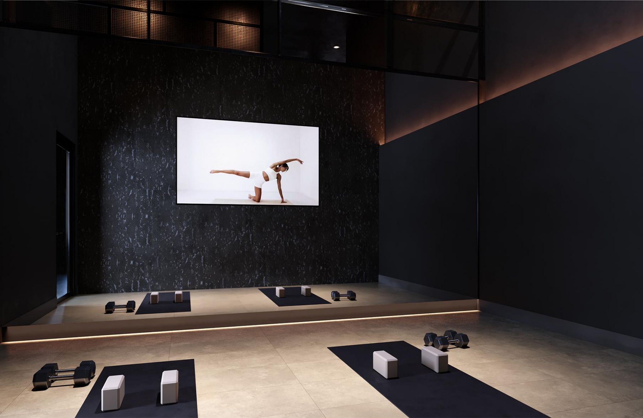 Modern fitness studio at Solana Central Park with dim lighting, weight training equipment, and a large screen displaying a yoga pose.