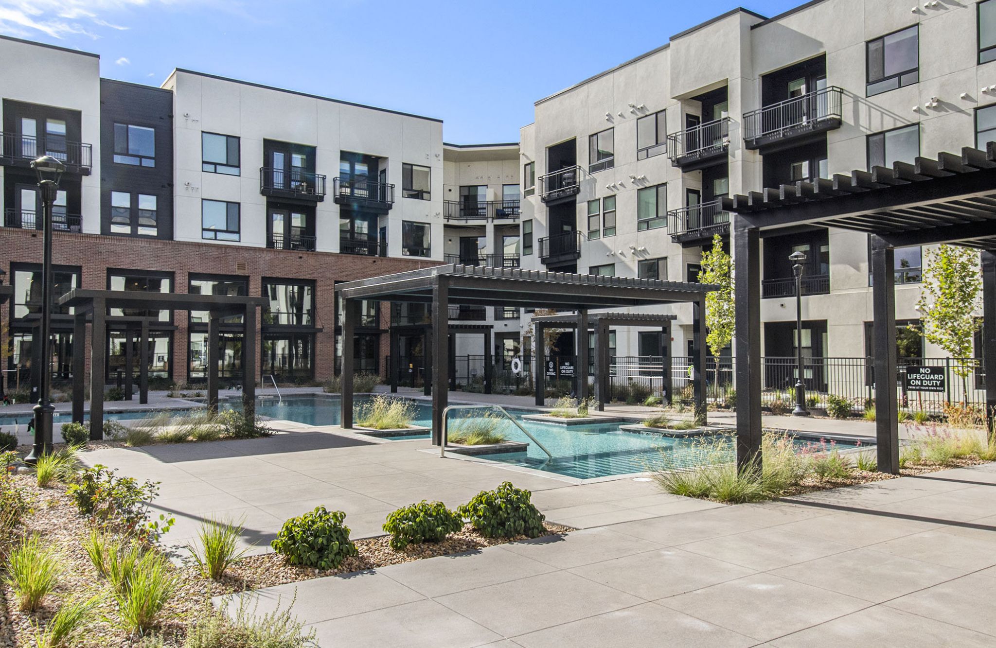 An outdoor view of Solana Central Park's pool area, surrounded by modern apartment buildings with black and white facades and pergolas framing the courtyard.