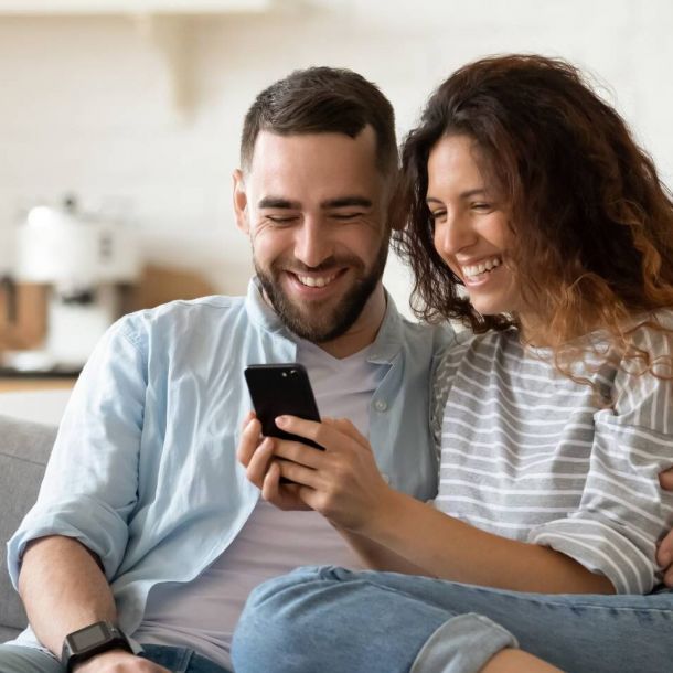 Happy couple looking at cellphone while relaxing on sofa in modern living room