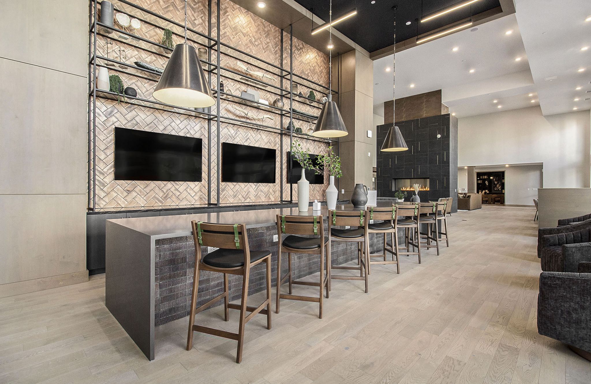 A modern lounge space in Solana Central Park featuring a communal table, wooden high chairs, pendant lighting, and decorative shelving with two large TV screens mounted on the wall.