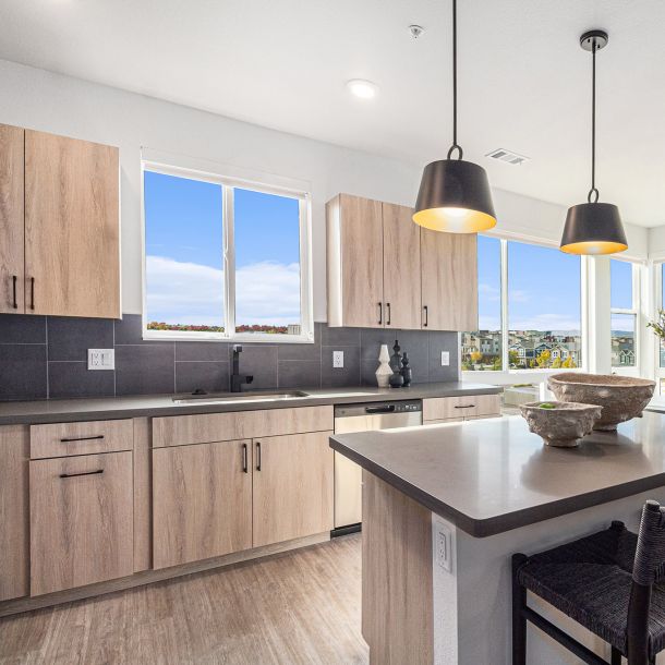 A bright kitchen in Solana Central Park with light wood cabinetry, black countertops, pendant lighting, and views from large windows.