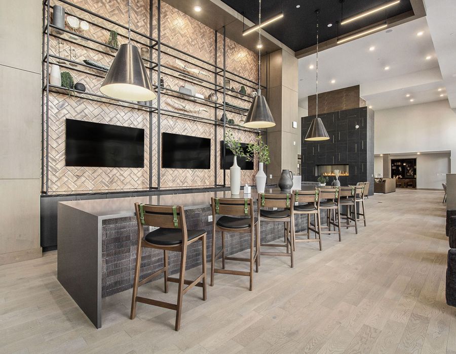 A modern lounge space in Solana Central Park featuring a communal table, wooden high chairs, pendant lighting, and decorative shelving with two large TV screens mounted on the wall.