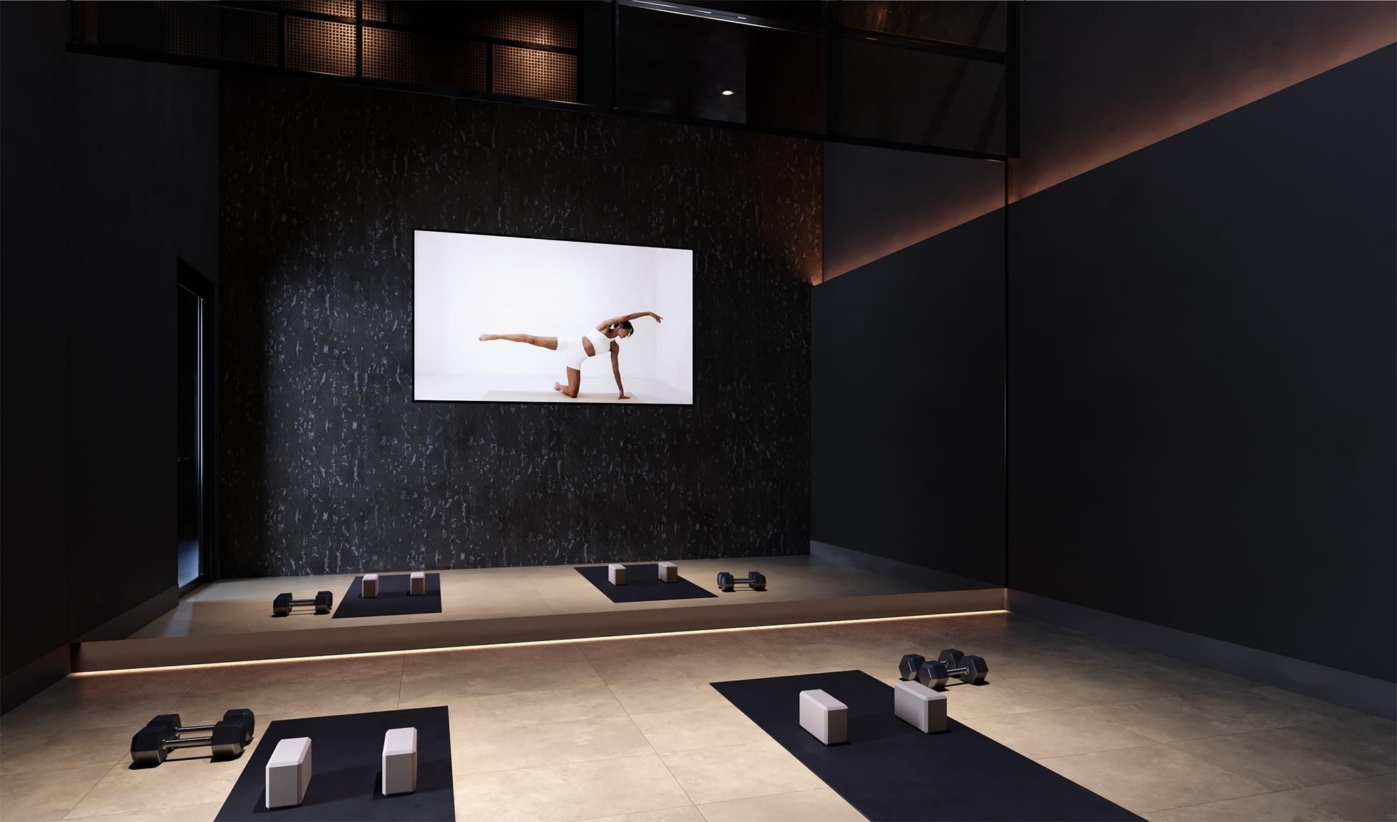 Modern fitness studio at Solana Central Park with dim lighting, weight training equipment, and a large screen displaying a yoga pose.