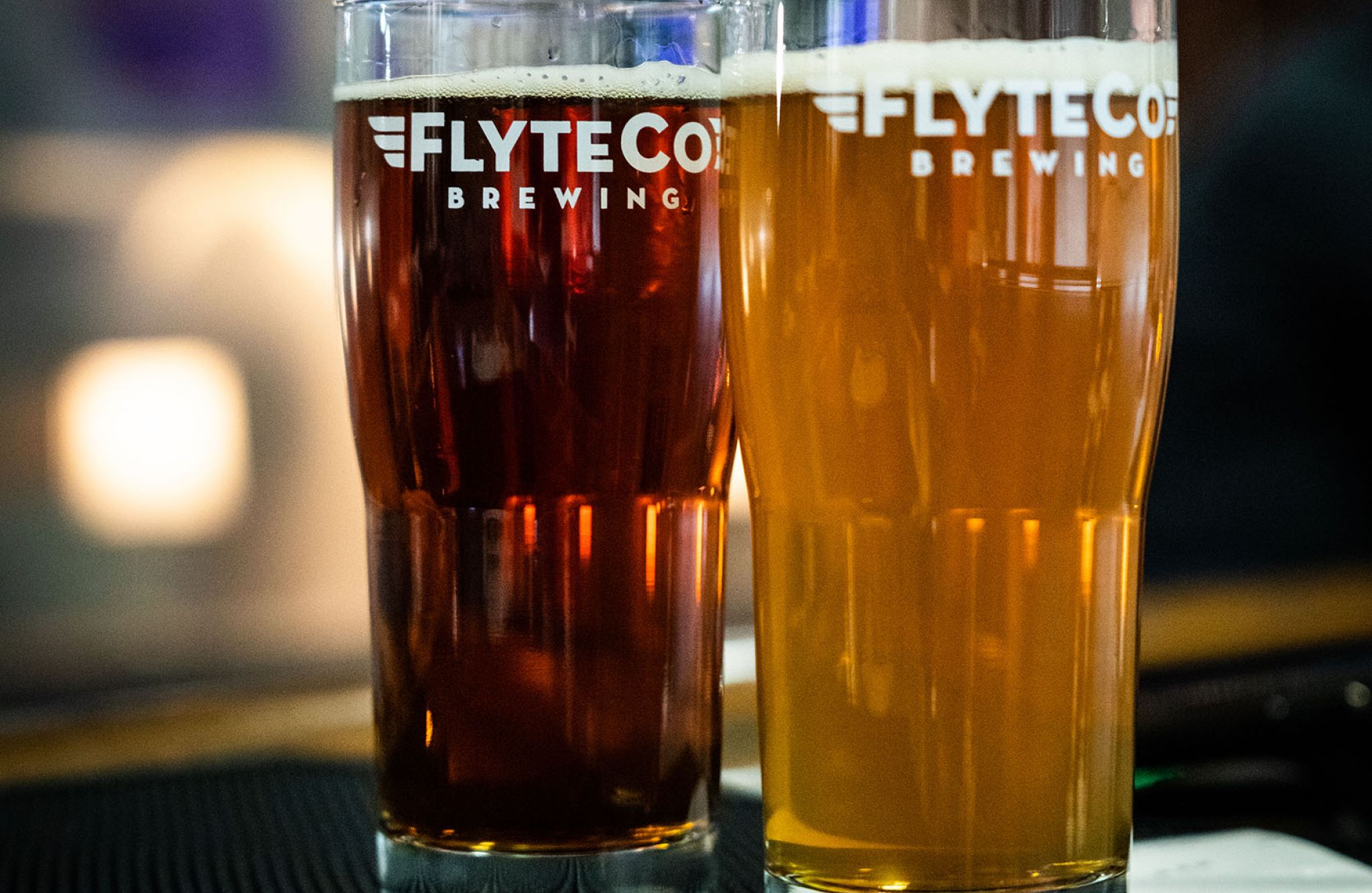 A light beer and a dark beer in pint glasses on a bar countertop