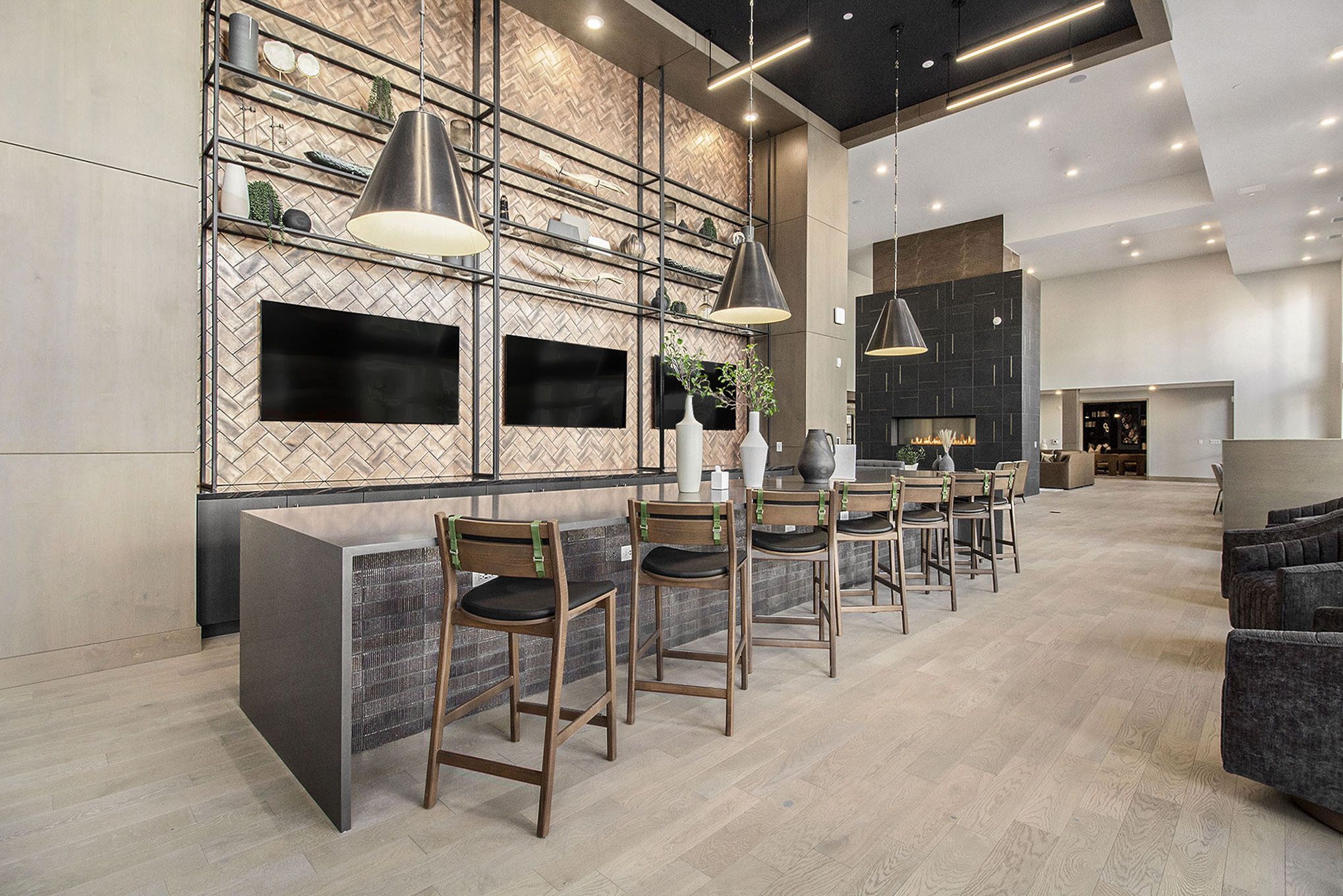 A modern lounge space in Solana Central Park featuring a communal table, wooden high chairs, pendant lighting, and decorative shelving with two large TV screens mounted on the wall.